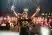 A man wearing a beanie on stage holds a microphone and raises his arms